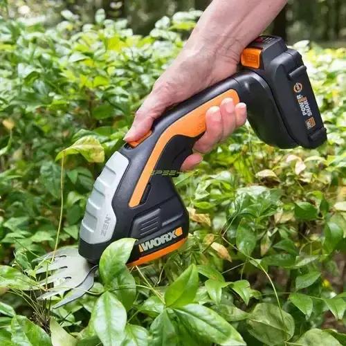 WG801E-WORX-CORDLESS-SHRUB-SHEAR-20V-3-BLADES-1 (1) Hand holding WG801E WORX cordless shrub shear 20V with 3 blades trimming green plants in garden setting